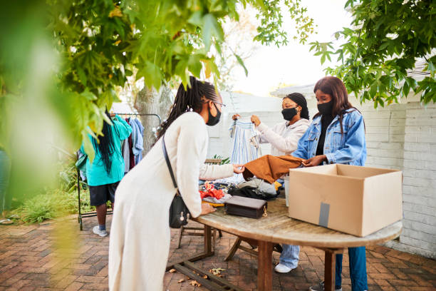 Teens in masks running a charitable second hand clothing sale Group of young African teenage girls in protective face masks running a second hand clothing yard sale to raise funds for charity clothing swap photos stock pictures, royalty-free photos & images