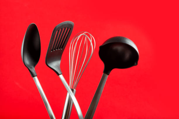 Black set of black and metal kitchen utensils on red background. Whisk, ladle, kitchen spatula.