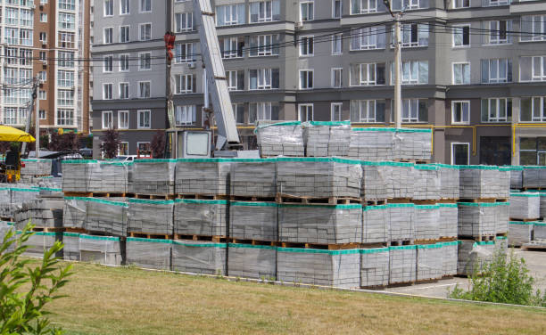 There are many new gray paving slabs on plastic-covered pallets on the construction site. Paving of pedestrian paths on a city street. Foreground. Repair of the sidewalk in the city square.