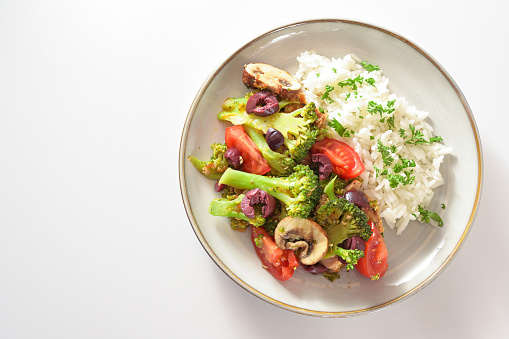Vegetarian meal from broccoli, tomatoes and olives with rice on a gray plate, cooking with healthy vegetables, light background with copy space, high angle view from above