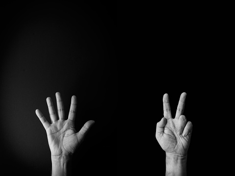 Dramatic black and white image of male hand demonstrating sign language number seven against black background with empty copy space for editors