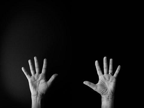 Dramatic black and white image of male hand demonstrating sign language number ten against black background with empty copy space for editors