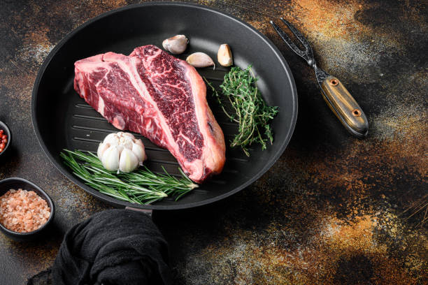 raw fresh meat t-bone steak with spices, garlic and rosemary, on frying cast iron pan, on old dark rustic background - veal t bone steak raw steak imagens e fotografias de stock