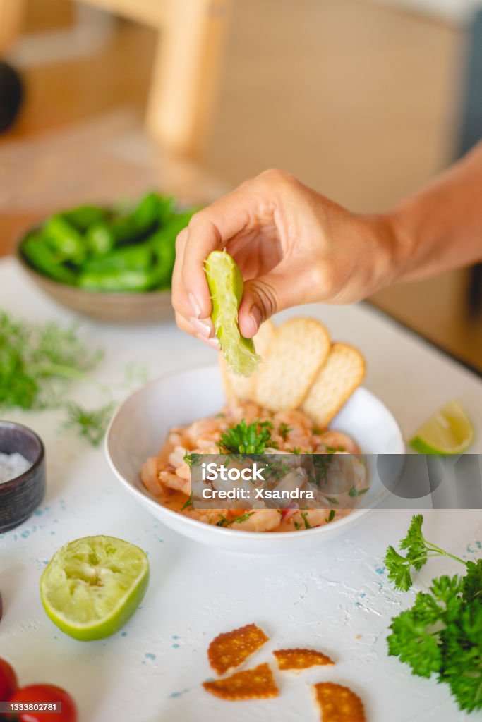 Hand adding lime juice to a bowl of shrimp ceviche Hand  squeezing lime juice onto a plate with shrimp ceviche Seviche Stock Photo
