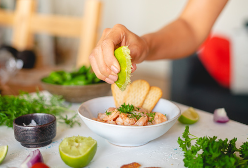 Hand  squeezing lime juice onto a plate with shrimp ceviche