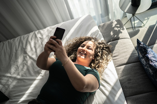 Happy woman using smartphone lying on the bed at home