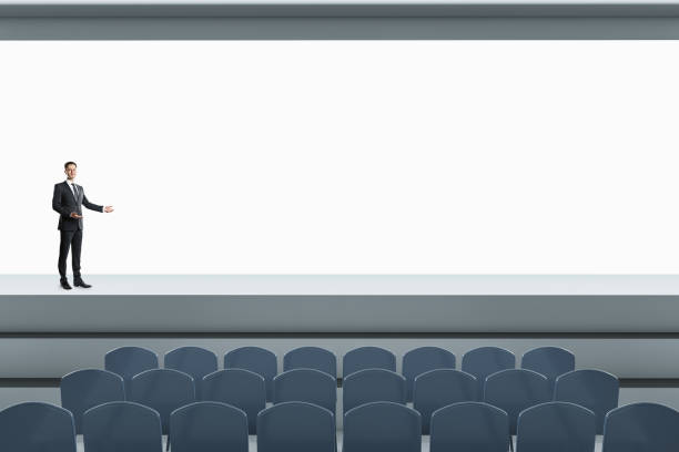 Dark empty cinema auditorium with blank white wide screen, rows of seats and red velvet curtains