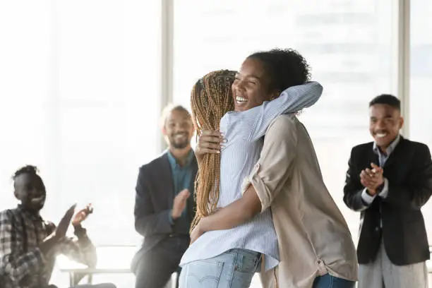 Photo of Happy young african ethnicity woman cuddling colleague.