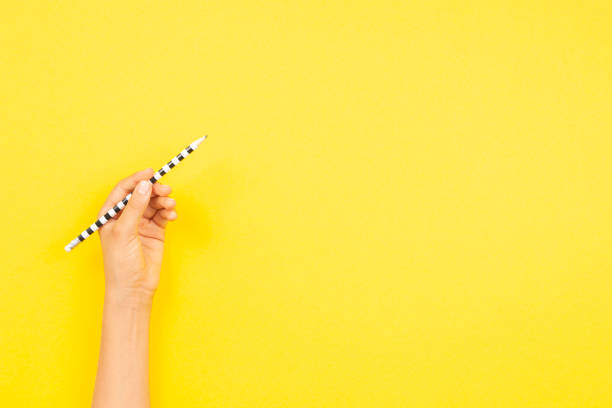 istock Left hand holding pencil for writing over yellow background. Top view, copy space for text. Left Handers Day 1333810705