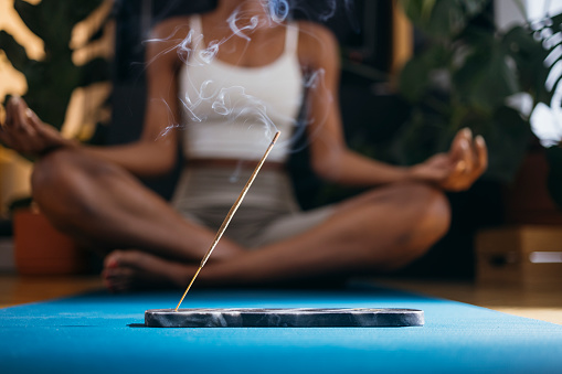 Unrecognizable African-American woman relaxing and enjoying incense stick on yoga class