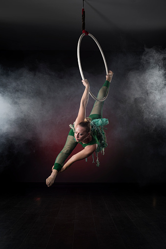 Aerial acrobat in the ring. \nA woman performs the acrobatic elements in the air ring.