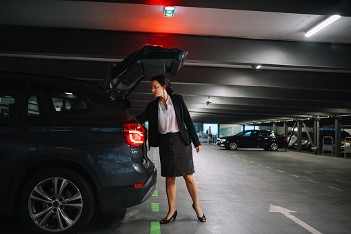 Portrait of a businesswoman walking out of her car in the parking garage. She is leaving it to charge in the garage.