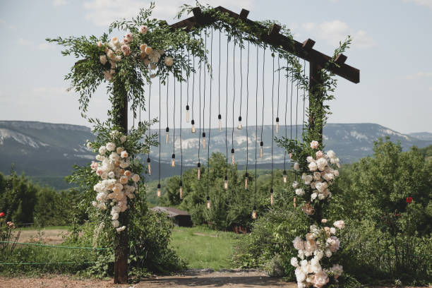 istock Wedding arch on boho style with white flowers in park with light bulbs. 1333820159