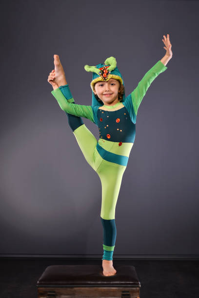 Amusing children (the girl dressed in a magician costume and the boy dressed in a strongman costume) are showing the circus performance. The preadolescent girl is smiling looking away. She is holding the magic wand in the hand. The girl is pointing the magic wand at the rabbit. The elementary age boy is holding the rabbit for it ears and he is hilding the fake barbell in other his hand. The strongman boy is smiling looking at the camera. Studio shooting on red background with glowing star and the striped theatrical curtain