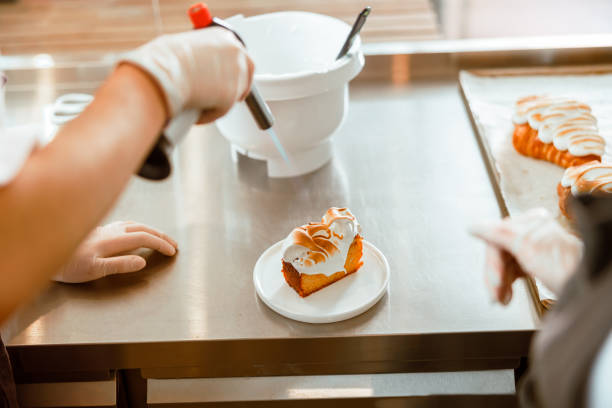 istock Professional confectioner makes pattern on cake with cream using gas burner at countertop 1333825613