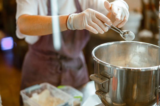 istock Baker in gloves pours powder ingredient into bowl making dough in workshop 1333825647