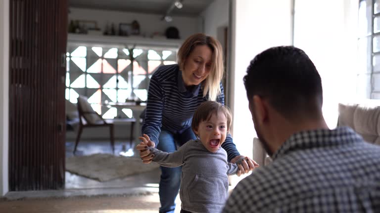 Parents helping and embracing son with special needs taking his firt steps at home