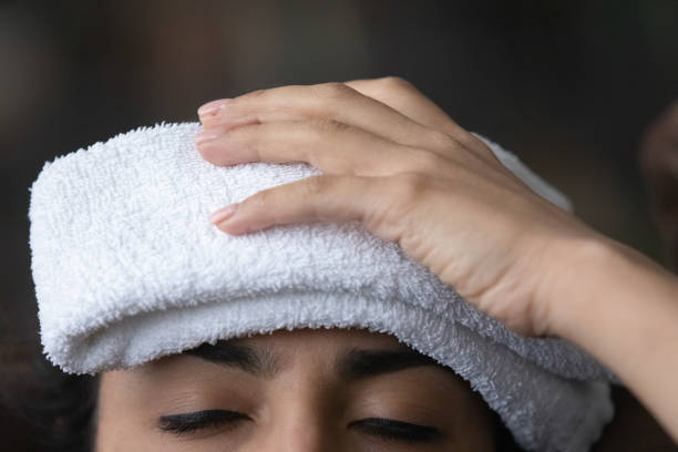 sick young female having fever holding wet towel on head - ice pack fotos imagens e fotografias de stock