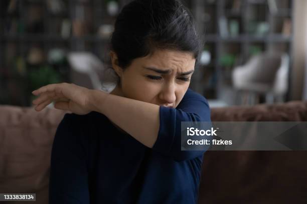 Sick Millennial Indian Woman Coughing Covering Mouth With Elbow Stock Photo - Download Image Now