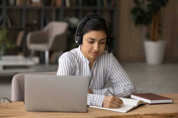 istock Ethnic female student in headphones take notes from online training 1333838154