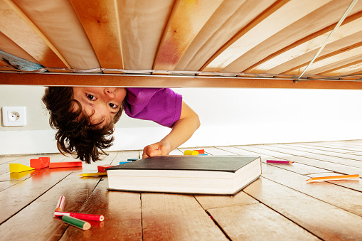 Boy finds book under the bed leaning down looking to camera