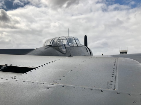 Photo of a WW2 era Grumman TBF Avenger plane, closeup of the tail looking towards the cockpit, backdrop is a dramatic cloudy sky.
