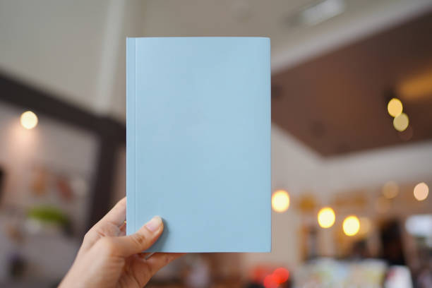 istock Woman's hand holding a light blue book with blank cover for inserting text on blurred cafe background. 1333861573