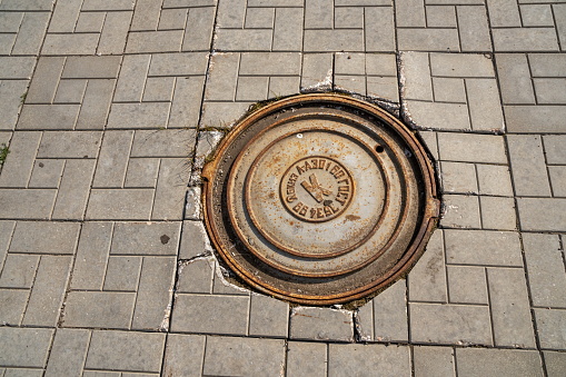 Krasnoyarsk, Krasnoyarsk Region, RF - July 19, 2021: A cast iron manhole cover is located on the pavement of gray concrete tiles.