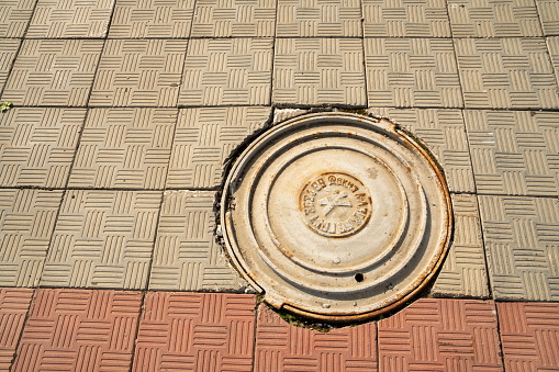 Krasnoyarsk, Krasnoyarsk Region, RF - July 19, 2021: Cast iron cover of the sewer manhole - part of the manhole cover is located on the pavement made of concrete slabs.