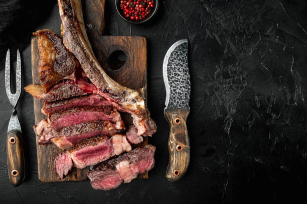 istock Grilled sliced tomahawk beef steak, on wooden serving board, on black stone background, top view flat lay 1333882667