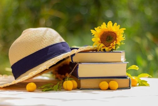 straw hat, sunflower flower on a stack of books on the table in the garden. rest, reading, vacation concept
