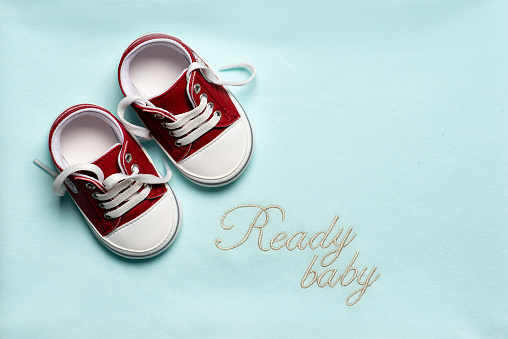 Red newborn baby boy or girl shoes on blue background with copy space and ready baby text