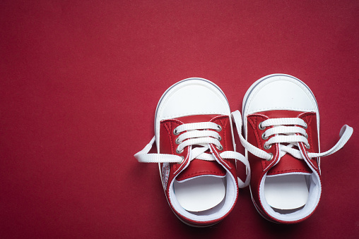 Red newborn baby boy or girl shoes on red background with copy space