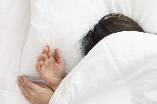 Woman lying in bed under white blanket in bedroom. Healthy sleep concept