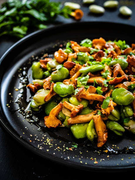 saubohnensalat mit gebratenen pfifferlingen, knoblauch und petersilie auf holztisch - fava bean stock-fotos und bilder