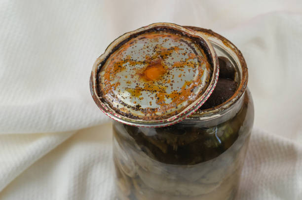 Opened Glass jar with homemade pickled mushrooms. Rusty tin lid with black spots. Spoiled blackened forest mushrooms. Botulism, food poisoning from canned foods concept.