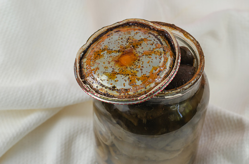 Opened Glass jar with homemade pickled mushrooms. Rusty tin lid with black spots. Spoiled blackened forest mushrooms. Botulism, food poisoning from canned foods concept.