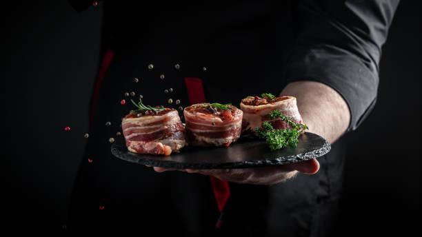 Cooking beef steak by chef hands. Medallions steaks from the beef tenderloin covered bacon on dark background. banner, menu recipe place for text stock photo