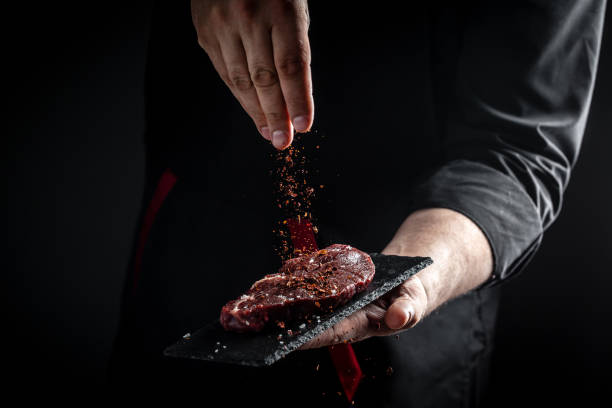 el chef cocina el bistec de carne y agrega condimentos en un movimiento de congelación. filete fresco de ternera prime black angus crudo. banner, receta de menú - bistec fotos fotografías e imágenes de stock