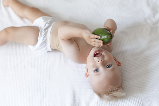 little boy blue-eyed with white hair is lying on the bed and holding an avocado in her hands