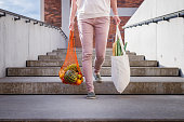 Woman walking at stairscase and holding reusable mesh bag after shopping groceries in city