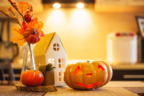 Kitchen decoration for Halloween: luminous cardboard house, candle, autumn leaves, persimmon, jack-o-lantern Kitchen decoration for Halloween and Autumn - luminous cardboard house, candle, bouquet with autumn leaves, persimmon, jack-o-lantern. halloween pumpkin decorations stock pictures, royalty-free photos & images