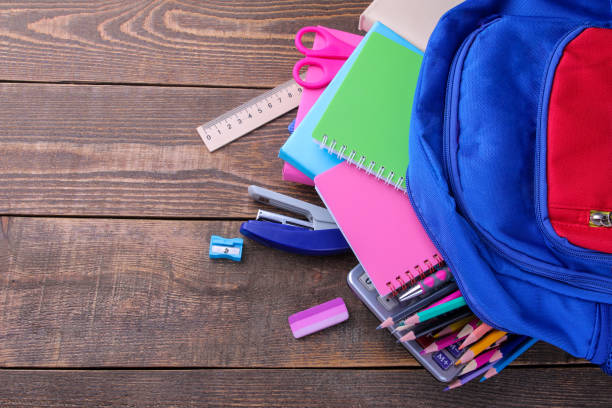 istock Different colored school accessories falling out of a school backpack on a brown wooden table 1333914181