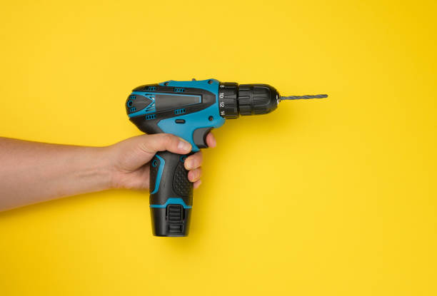 istock female hand holds a cordless drill on a yellow background. Tool for work 1333916079