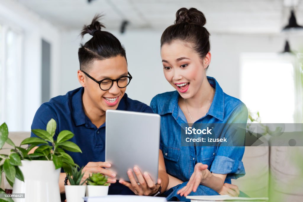 Friends discussing over digital tablet in the office Asian business people discussing over digital tablet at table. Male and female colleagues are sitting at creative workplace. They are in smart casuals in office. 25-29 Years Stock Photo