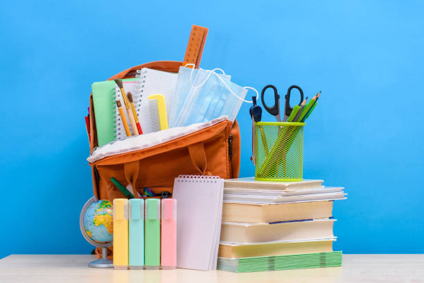 istock Preparing children for school. School items and textbooks next to a full school backpack 1333918579