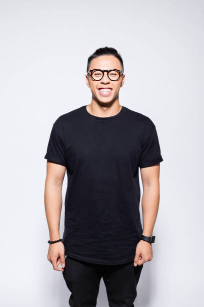 Cheerful asian young man in black clothes Portrait of handsome asian young man wearing black t-shirt, pants and eyeglasses, laughing at camera. Studio shot, grey background. black nerd stock pictures, royalty-free photos & images