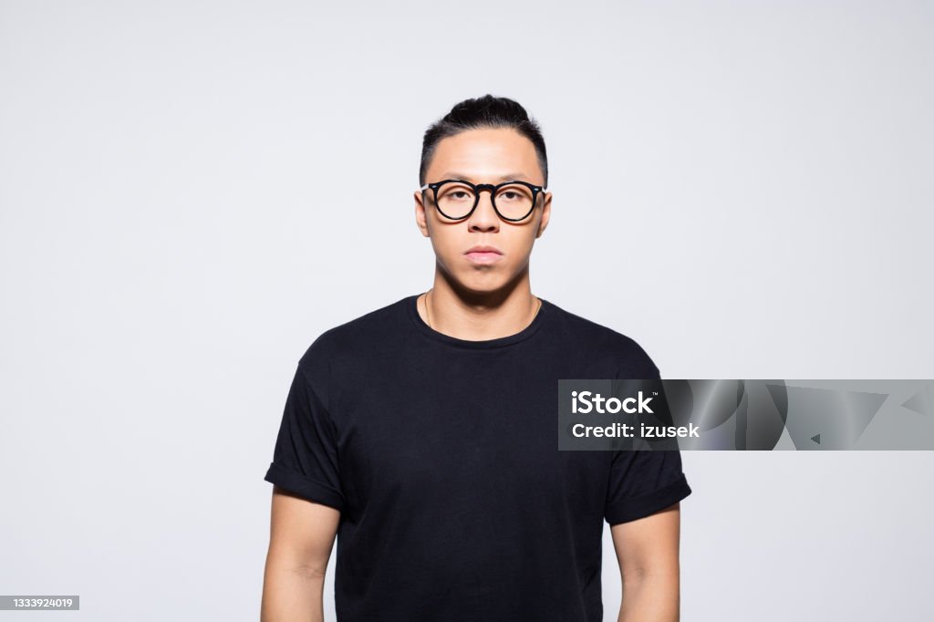 Confident asian young man in black clothes Portrait of handsome asian young man wearing black t-shirt and eyeglasses, looking at camera. Studio shot, grey background. 20-24 Years Stock Photo