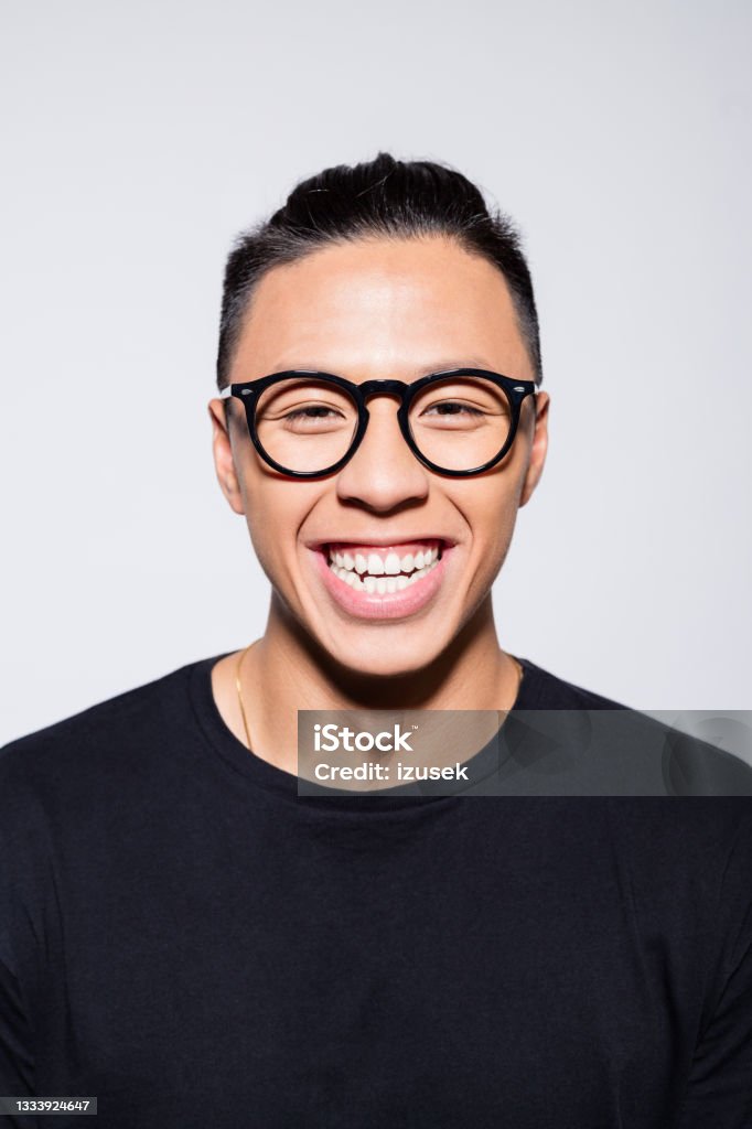 Excited asian young man in black clothes Headshot of happy asian young man wearing black t-shirt and eyeglasses, laughing at camera. Studio shot, grey background. Ecstatic Stock Photo