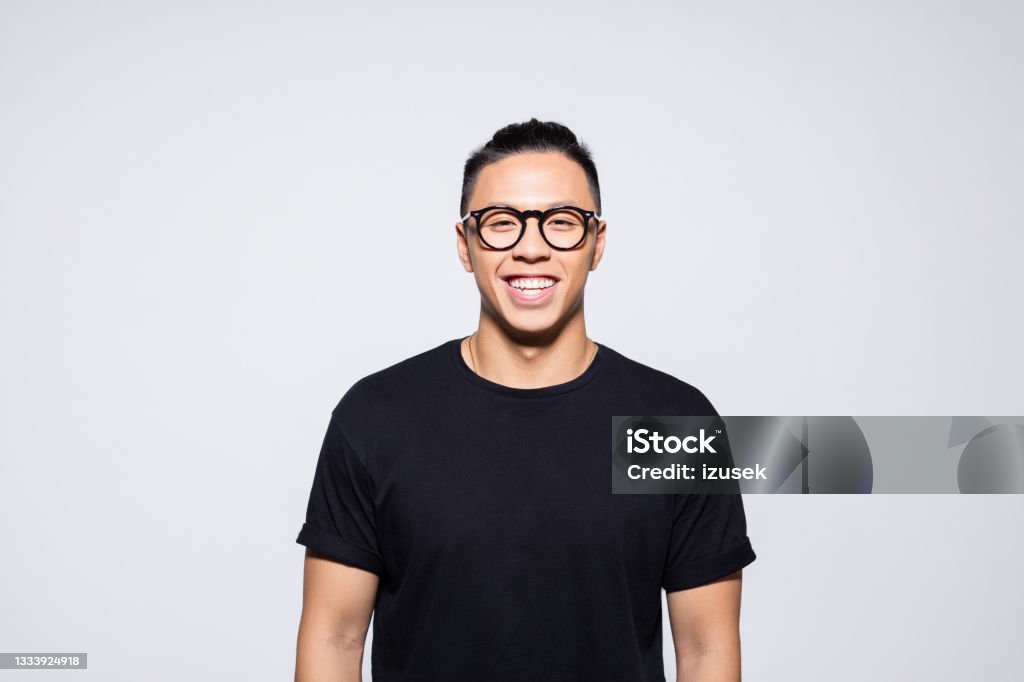 Happy asian young man in black clothes Portrait of handsome asian young man wearing black t-shirt and eyeglasses, smiling at camera. Studio shot, grey background. 20-24 Years Stock Photo
